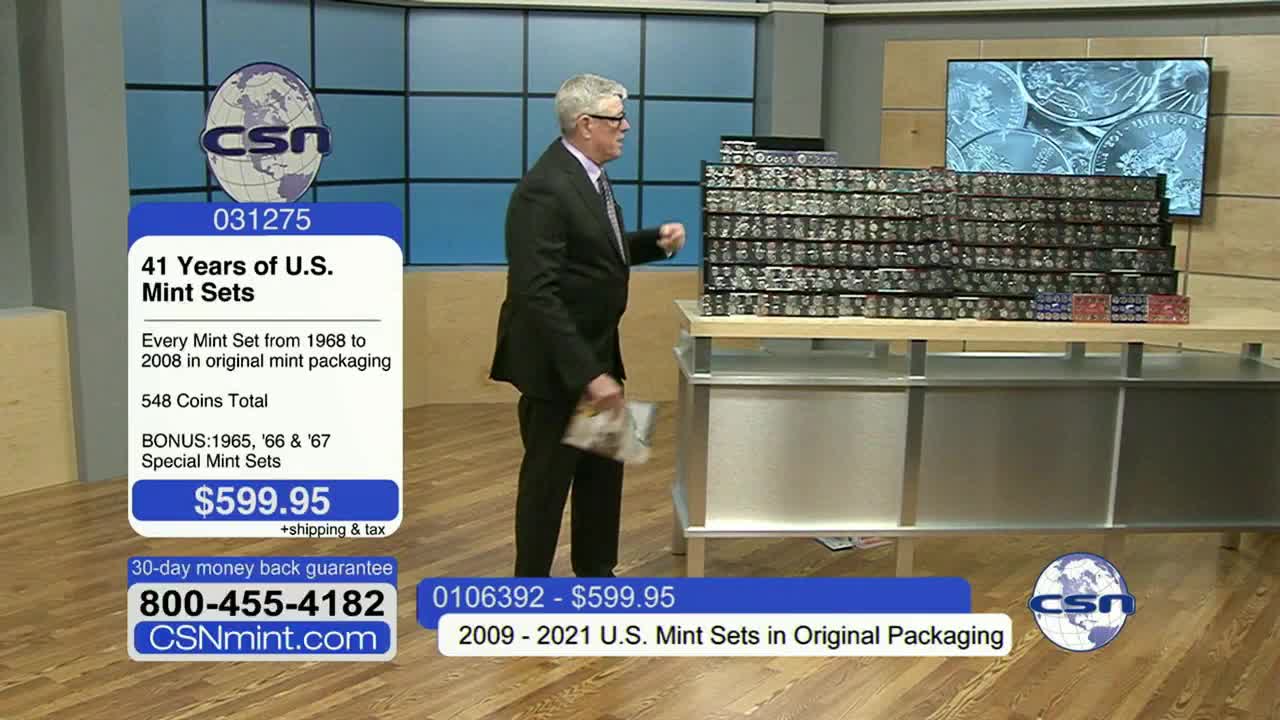 A man in a suit walks near a table stacked with what looks like coin sets, possibly on Fox Business Network. The screen shows a graphic advertising United States mint sets for sale.

