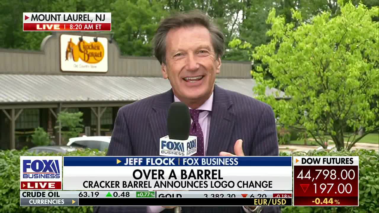 A Fox Business Network reporter in a suit smiles, standing in front of a Cracker Barrel restaurant in Mount Laurel, New Jersey. The bottom of the screen displays stock market information and the headline "Over a Barrel."
