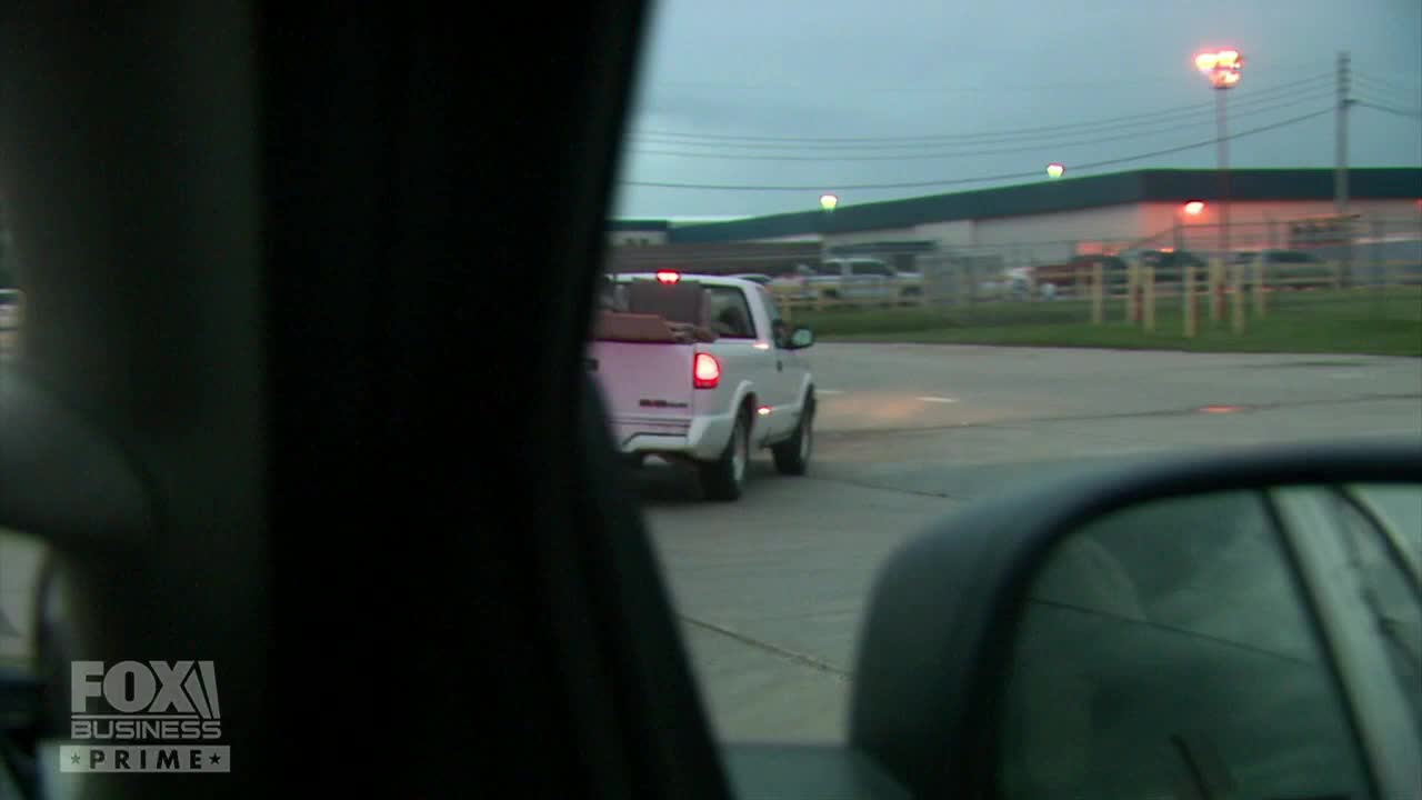 A white pickup truck is slowly pulling away, its taillights glowing against the overcast sky. The Fox Business Network logo is visible in the bottom left corner, suggesting this scene is part of a report from the United States.
