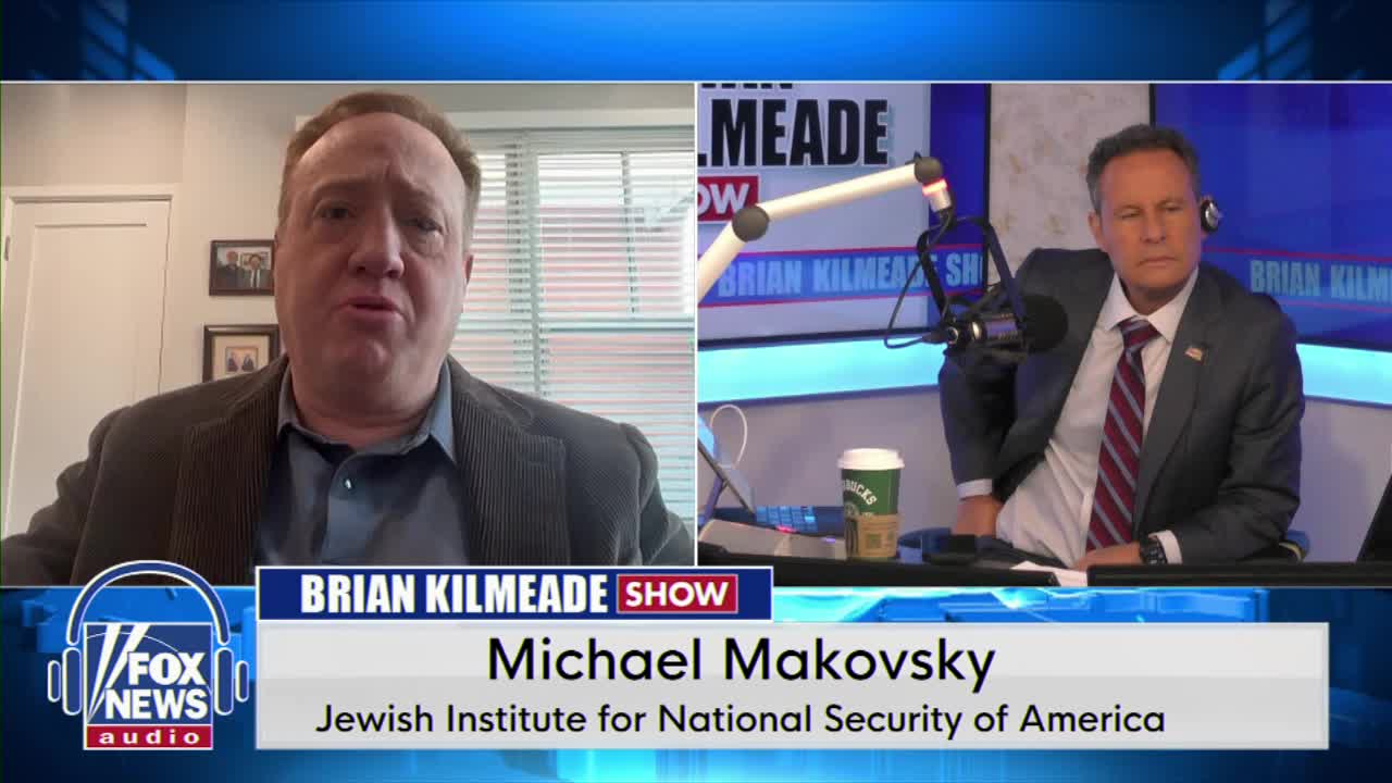 A man on a video call speaks animatedly, his face filling the left side of the screen. Beside him, a man in a suit sits at a radio desk, listening intently.