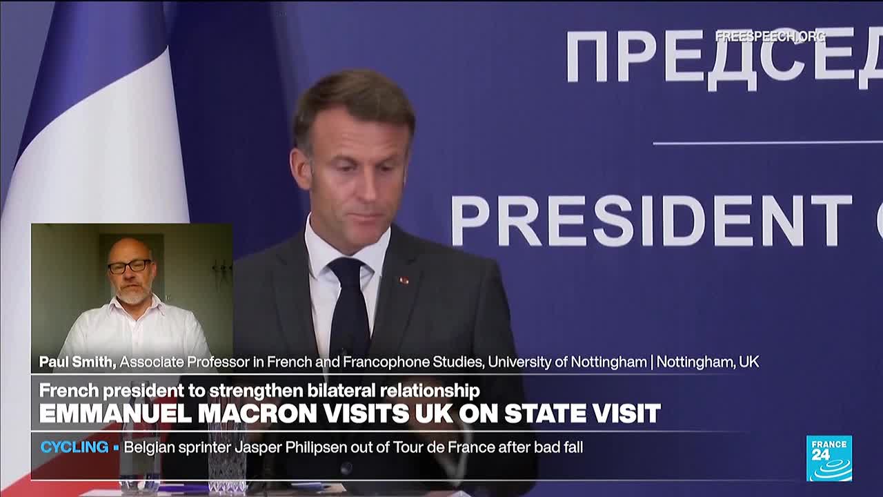Macron, in a dark suit and tie, speaks from behind a podium, the French flag visible to his left. A smaller screen shows a man in glasses, presumably an expert, offering commentary on the visit.
