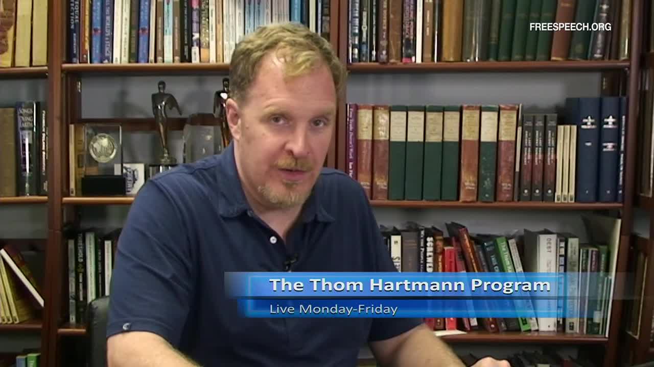 A man with reddish hair and a goatee is speaking directly to the camera, framed by bookshelves. The lower third of the screen identifies the show as "The Thom Hartmann Program" on Free Speech TV.
