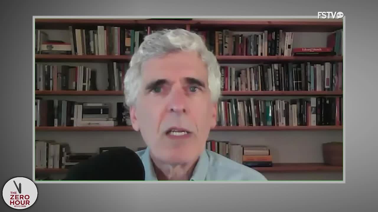A man with gray hair and a light blue shirt is speaking, his face framed by a bookshelf. He's on a broadcast for Free Speech TV, part of *The Zero Hour*.
