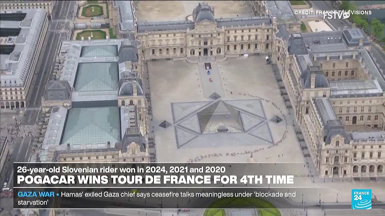 From a high angle, a few cyclists are visible riding in the courtyard of a large building. The news ticker on Free Speech TV reports the Tour de France winner.
