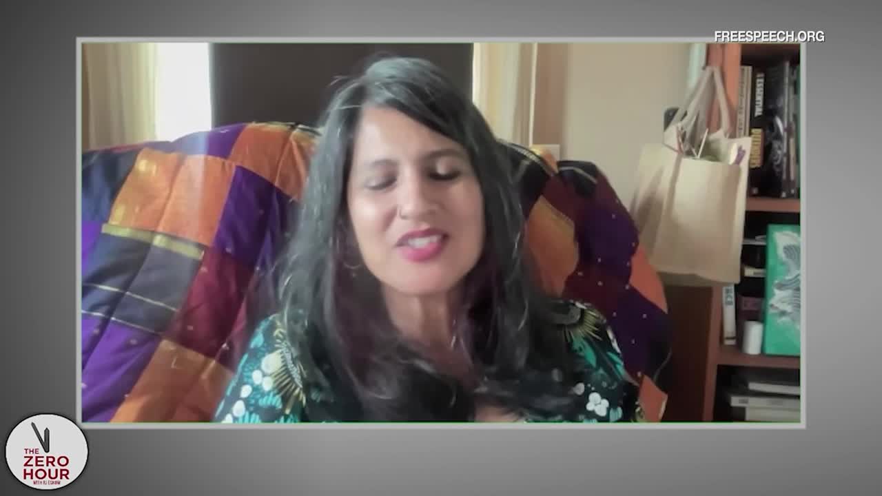 A woman with long, dark hair speaks directly to the camera, her lips moving as she forms words. The Free Speech TV logo is visible in the corner, and the background shows a cozy home setting.
