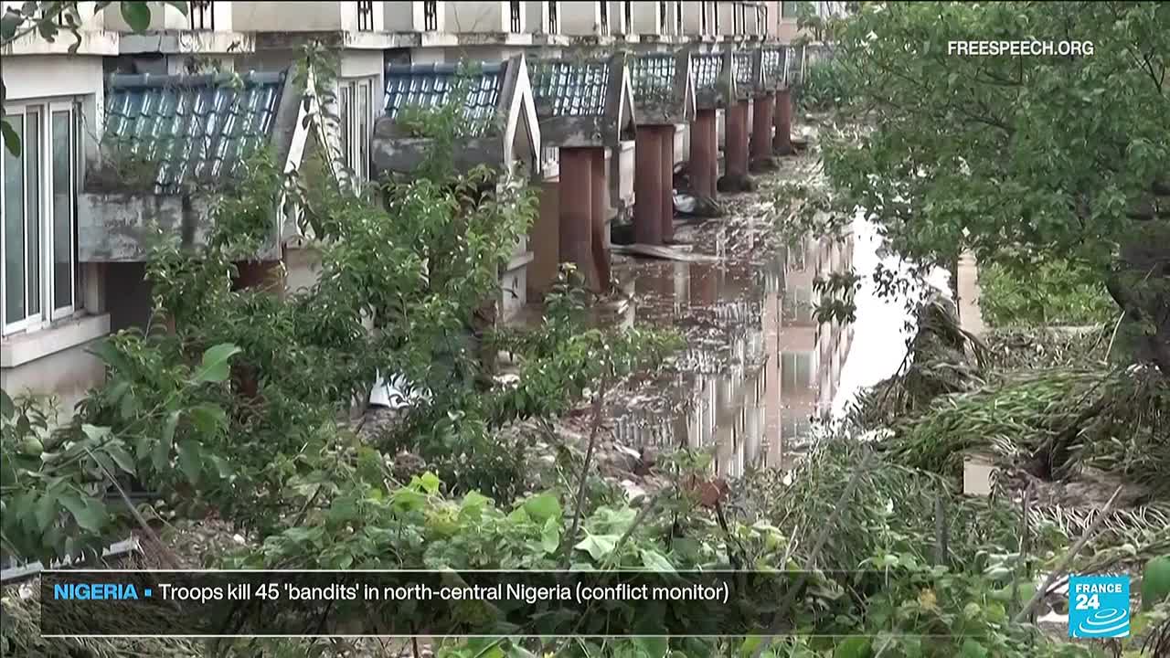 The camera angle looks across a flooded area, with water reflecting the buildings and trees. A news report from France 24, via Free Speech TV, is reporting on Nigeria.
