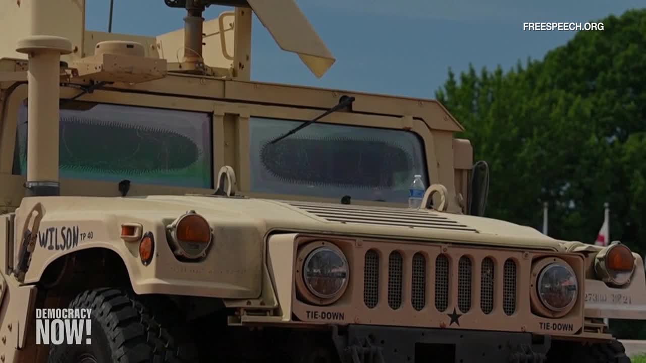 A large, tan military vehicle sits parked, its windshield reflecting a distorted view of the surroundings. The vehicle's name, "Wilson," is painted on its side.
