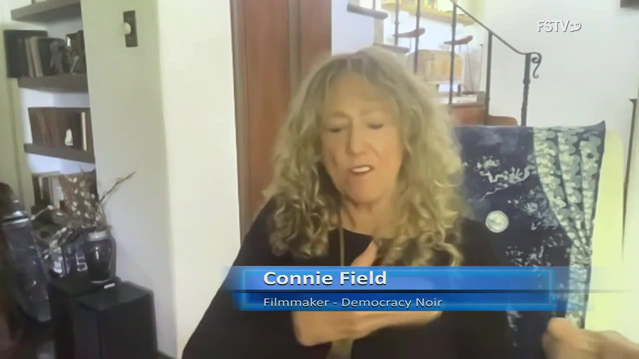 Connie Field, a filmmaker, is speaking on Free Speech TV, gesturing with her hands. The camera focuses on her, with a backdrop of a home interior.
