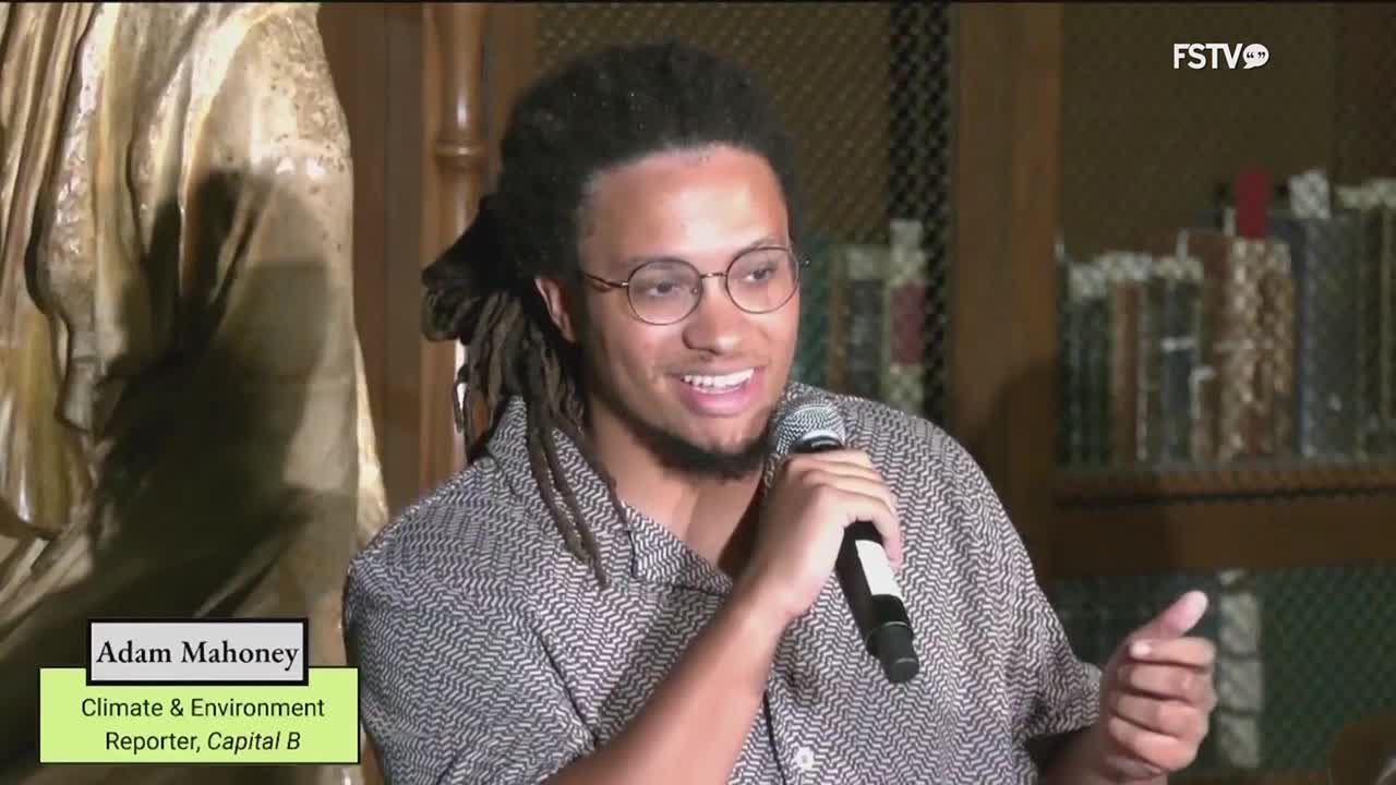 Adam Mahoney, a Climate & Environment reporter for Capital B, is speaking into a microphone on Free Speech TV. He's gesturing with his right hand as he talks, and the FSTV logo is in the top right corner.
