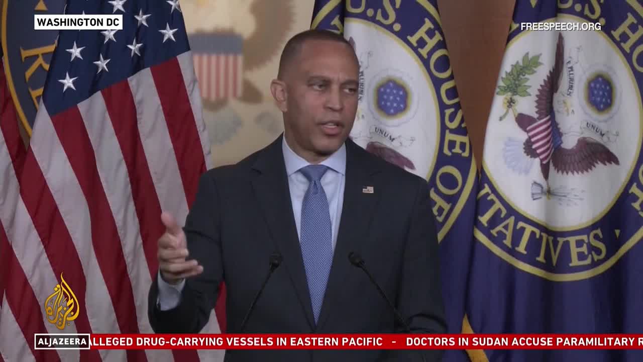 A man in a suit gestures with his hands as he speaks, the backdrop displaying the flags of the United States and the House of Representatives. The broadcast originates from Washington, D.C., and is being aired by Free Speech TV.

