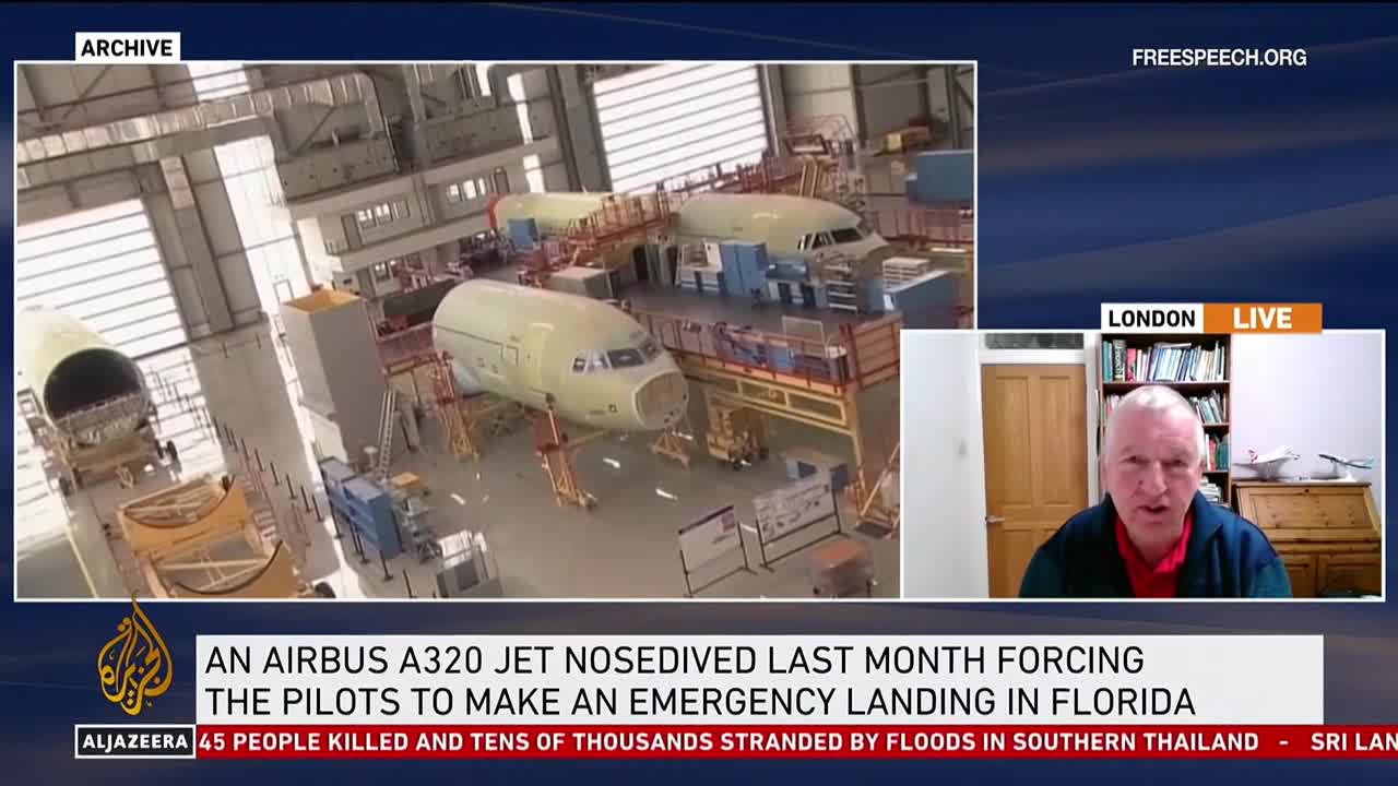 A man in London speaks on Free Speech TV, the Al Jazeera logo visible below. Behind him, a news segment shows an airplane hangar in the United States, with partially assembled aircraft.
