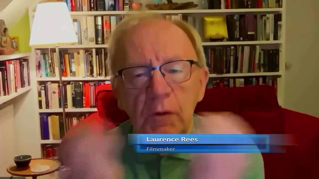 The man with glasses is speaking, his hands gesturing slightly as he sits in front of a bookshelf. A lower third identifies him as Laurence Rees, a filmmaker.
