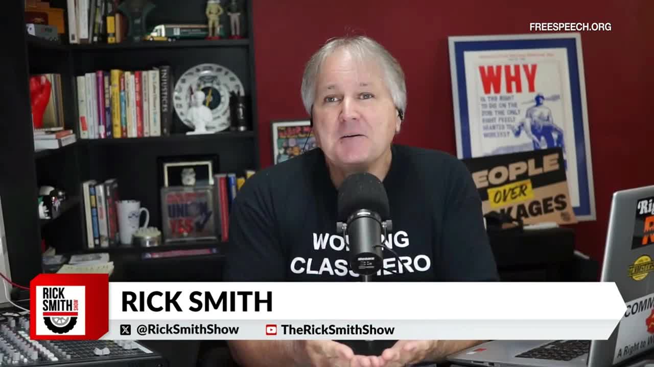 Rick Smith, on Free Speech TV, sits in front of a microphone, speaking to the camera. Behind him, a shelf is filled with books and various objects.
