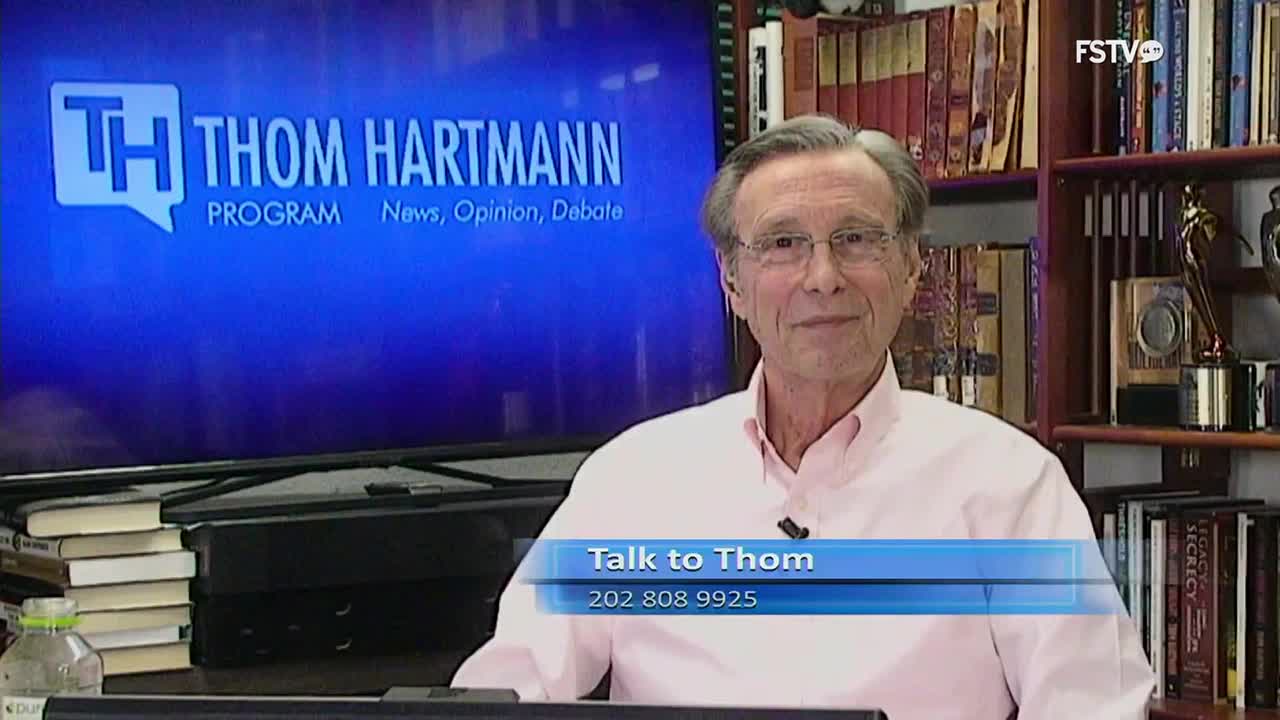 Thom Hartmann smiles directly at the camera, a blue graphic overlaying the bottom of the screen reads "Talk to Thom" with a phone number. Behind him, a large screen displays "TH THOM HARTMANN PROGRAM News, Opinion, Debate."