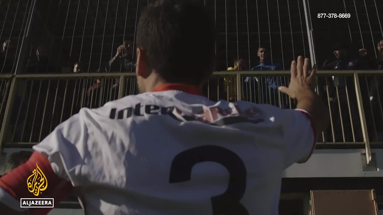 A man in a white jersey with the number 3 on the back raises his hand toward a crowd behind a railing. People in the stands watch him, some holding up their own hands.