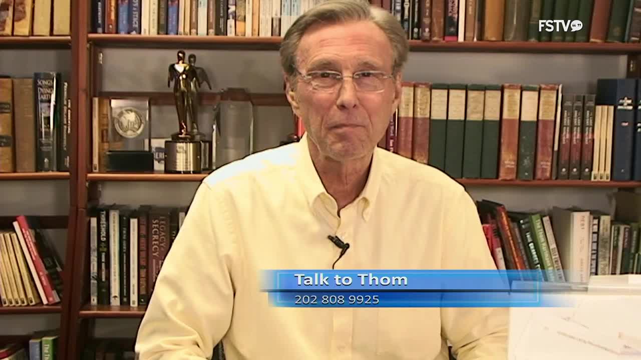 A man in a light yellow shirt speaks directly to the camera, a microphone clipped to his collar. Behind him, bookshelves overflow with volumes, a testament to a life of learning.