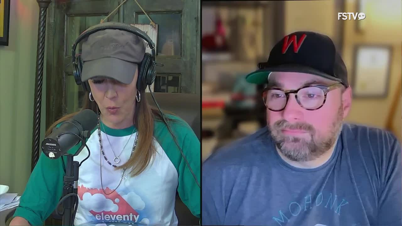 A woman with headphones and a baseball cap leans into a microphone, speaking. Across from her, a man in a baseball cap and glasses looks towards the camera.