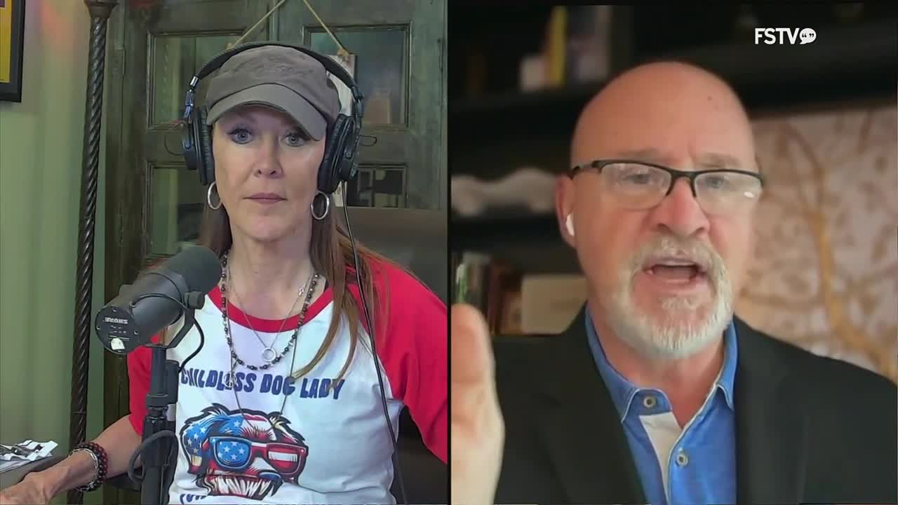 A woman with headphones and a baseball cap listens intently, a microphone in front of her. Across from her, a man in a suit speaks with his mouth open, his hand raised.