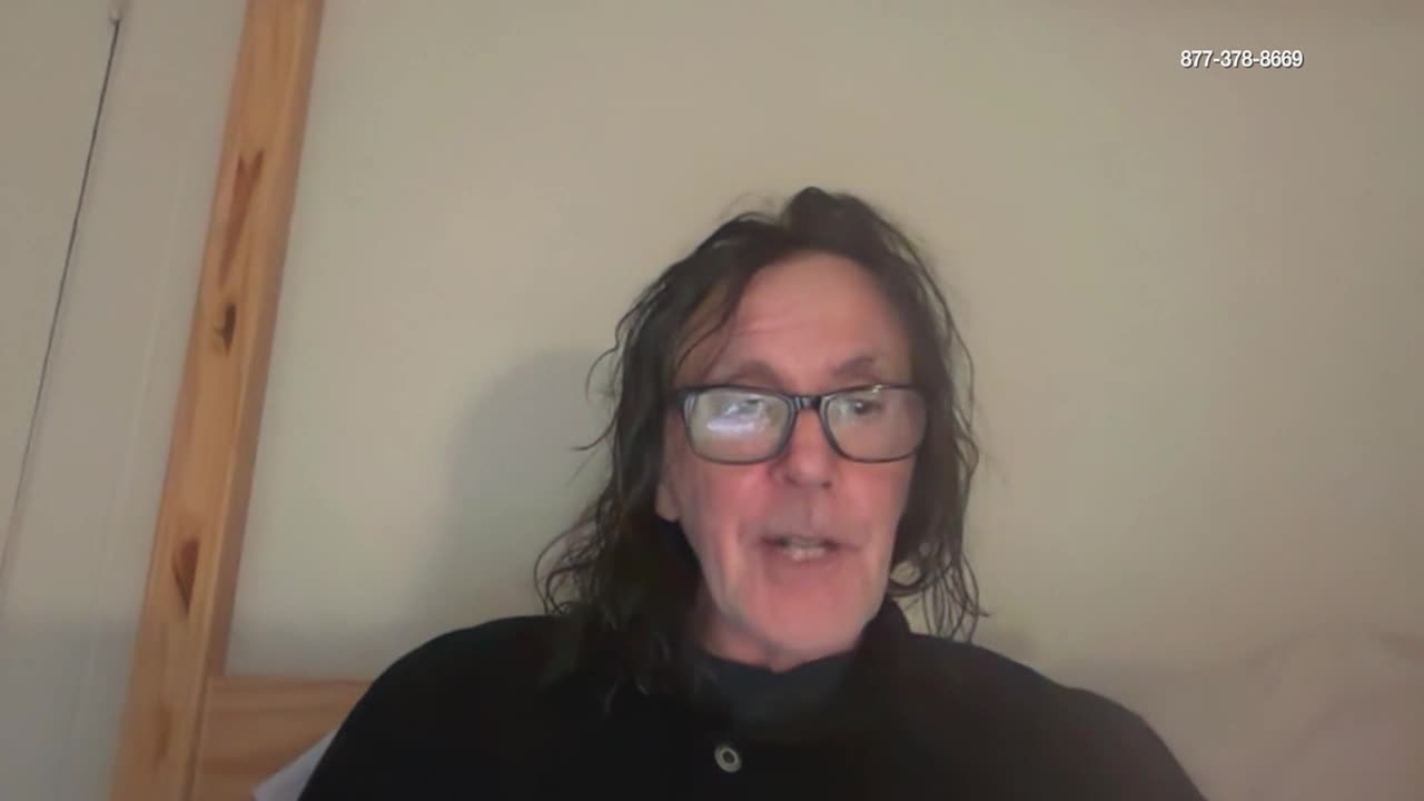 A man with dark, wavy hair and glasses speaks directly to the camera. A phone number is displayed in the upper right corner of the screen.