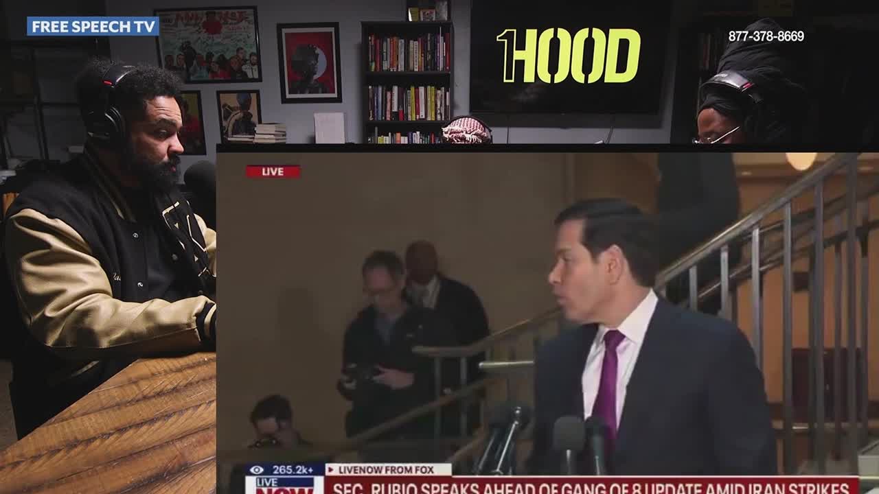 Senator Marco Rubio, in a dark suit and purple tie, speaks into a microphone. He appears to be walking down a staircase, with other people in the background.