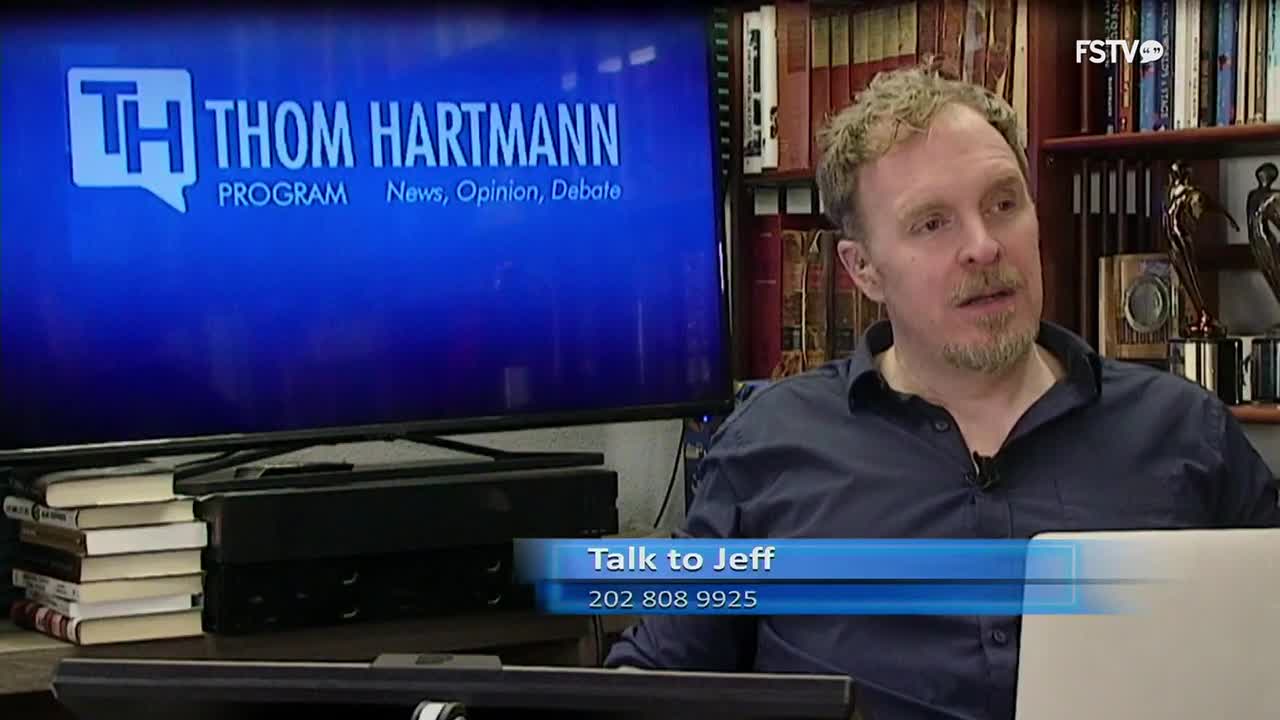 A man with curly hair is speaking, his gaze directed slightly off-camera. Behind him, a large screen displays the "Thom Hartmann Program" logo, and bookshelves are packed with volumes. A graphic overlay reads "Talk to Jeff" with a phone number.