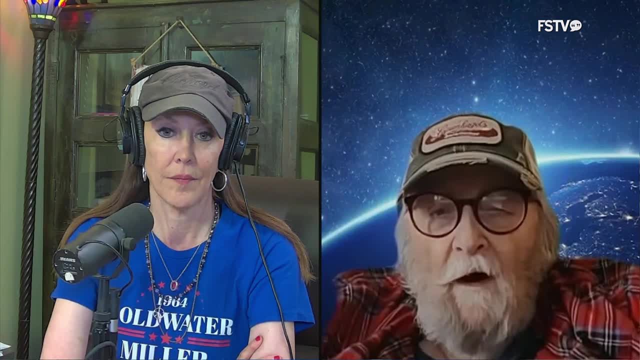 A woman in a blue shirt and baseball cap speaks into a microphone. Across from her, a man with a beard and glasses talks, his background a view of Earth from space.