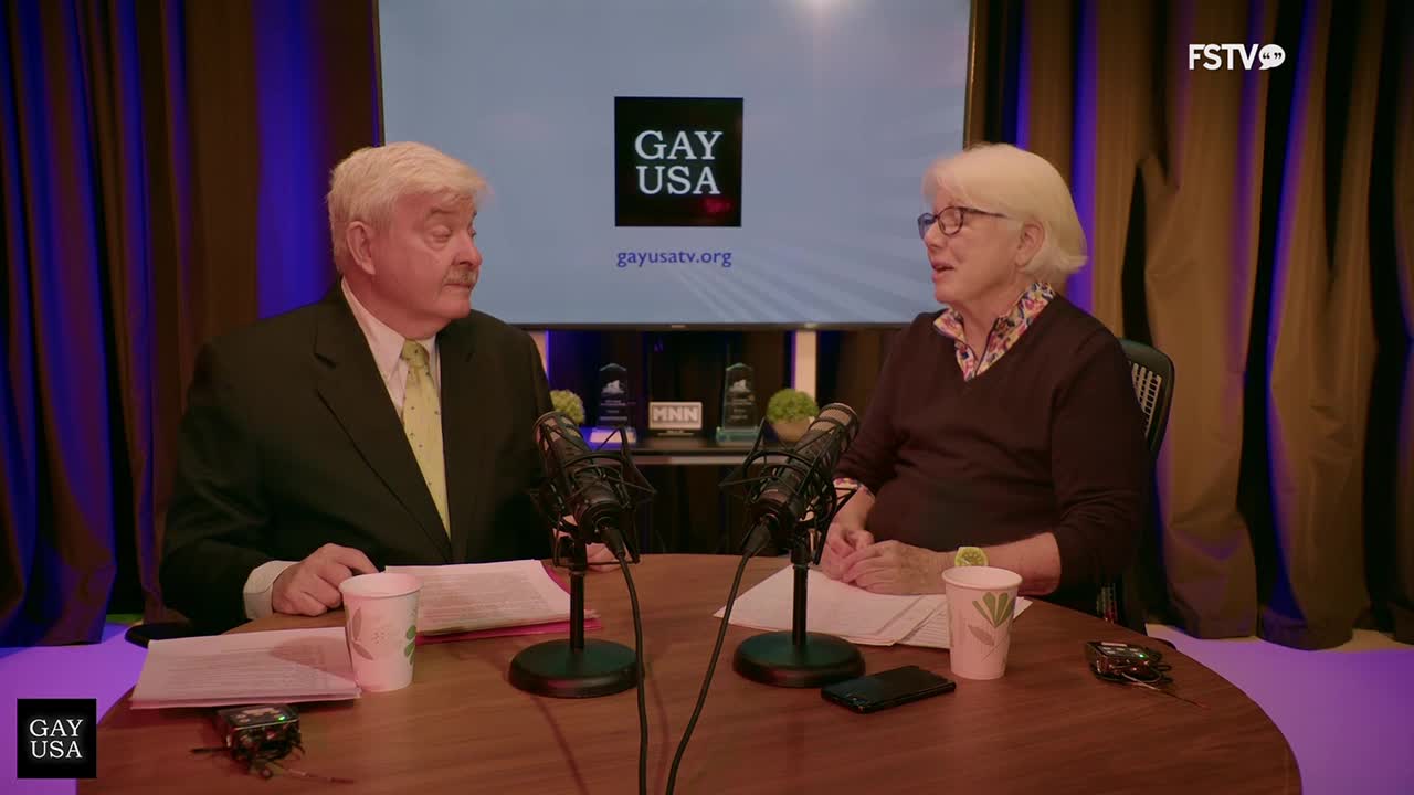 Two people sit at a table with microphones in front of them, discussing something for Gay USA. The Free Speech TV logo is visible in the corner.