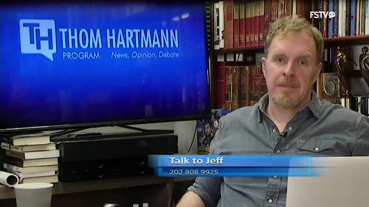 A man with a beard and a blue shirt sits in front of a large screen displaying the "Thom Hartmann Program" logo. A blue banner at the bottom of the screen reads "Talk to Jeff" with a phone number.