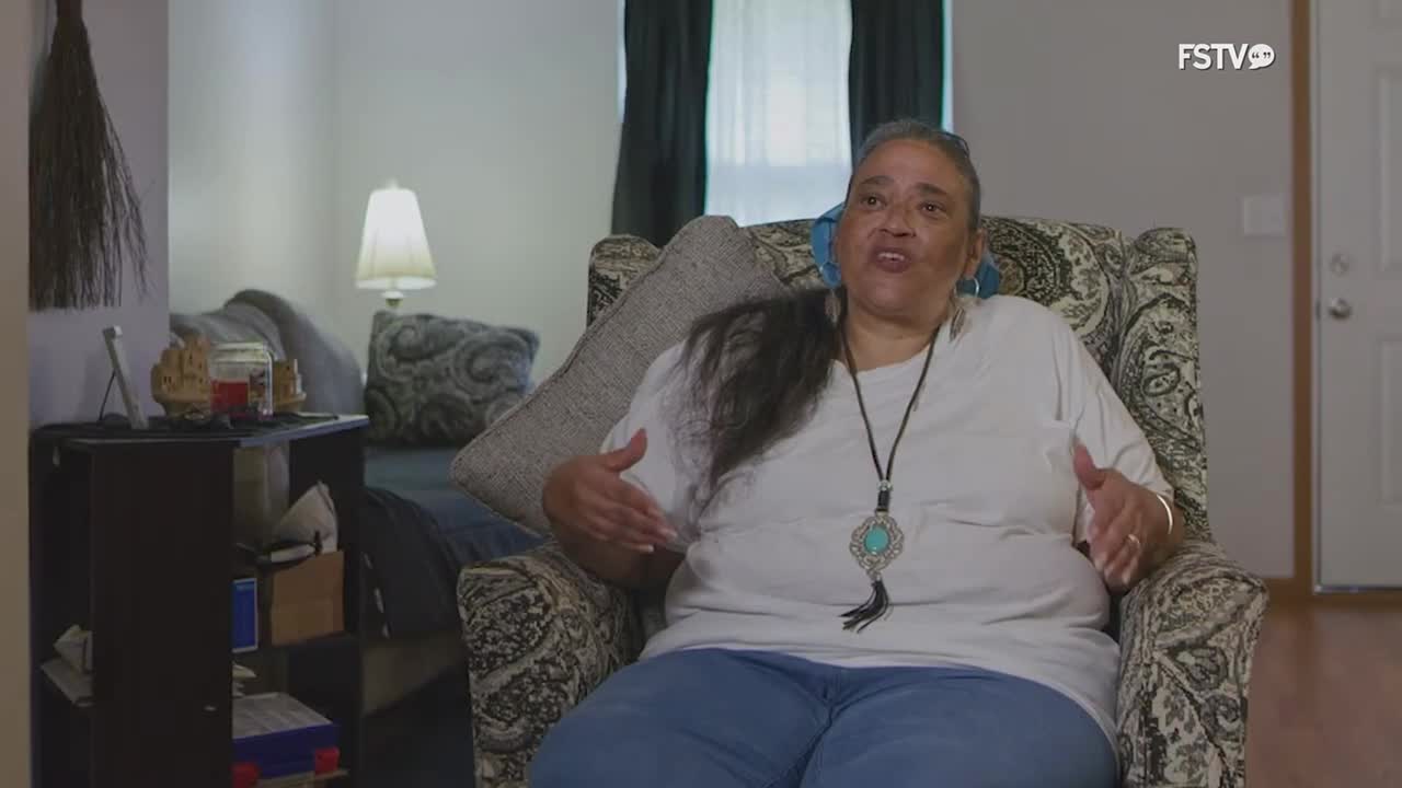 A woman speaks with her hands, gesturing as she sits in a patterned armchair. The FSTV logo appears in the corner of the screen.
