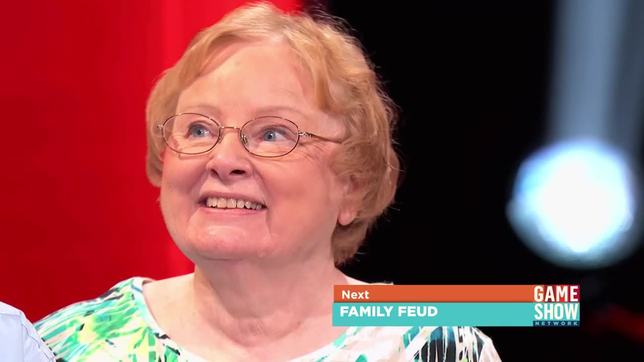 A woman in glasses smiles, her eyes looking upward. A "Family Feud" graphic and the Game Show Network logo are visible in the corner.
