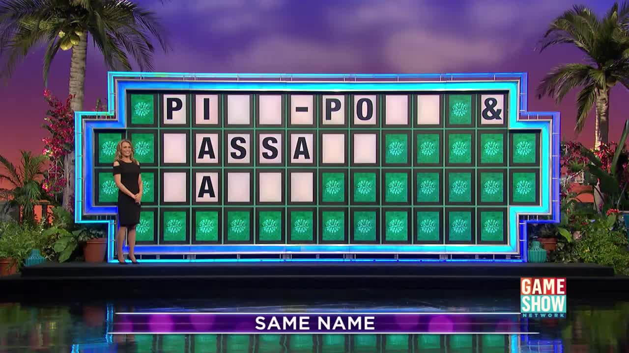A woman in a black dress stands beside a puzzle board on the Game Show Network stage. The board displays a partially revealed phrase, with the category "SAME NAME" displayed below.
