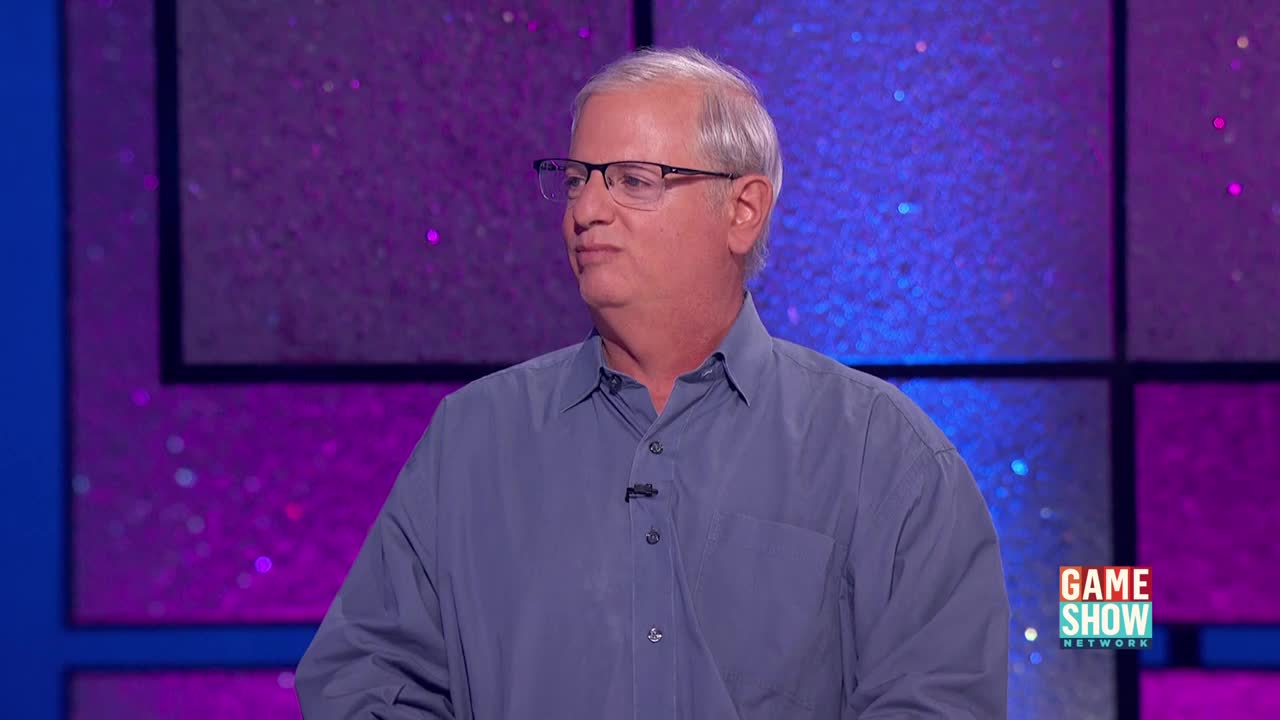 The man in the blue shirt is looking off to the side, his expression thoughtful. A "Game Show Network" logo is visible in the corner of the screen.

