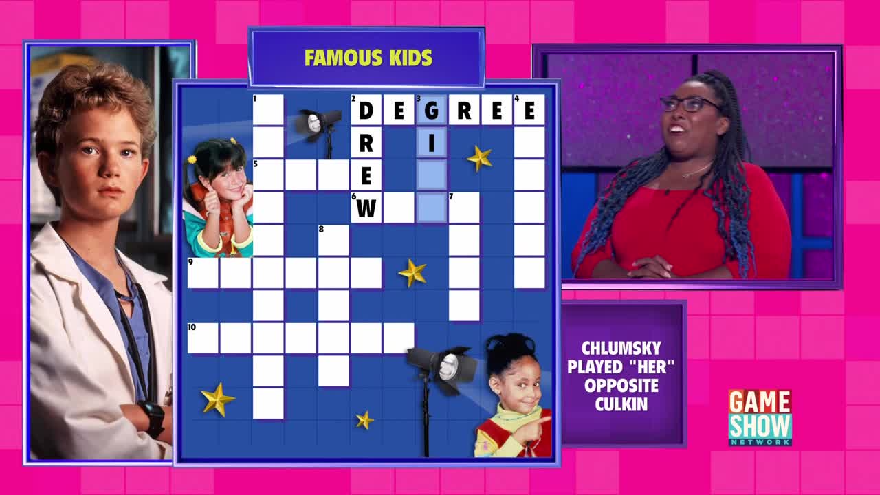 A contestant on the Game Show Network is standing in front of a crossword puzzle themed around "Famous Kids." The host, wearing a red top, seems to be reacting to a clue.

