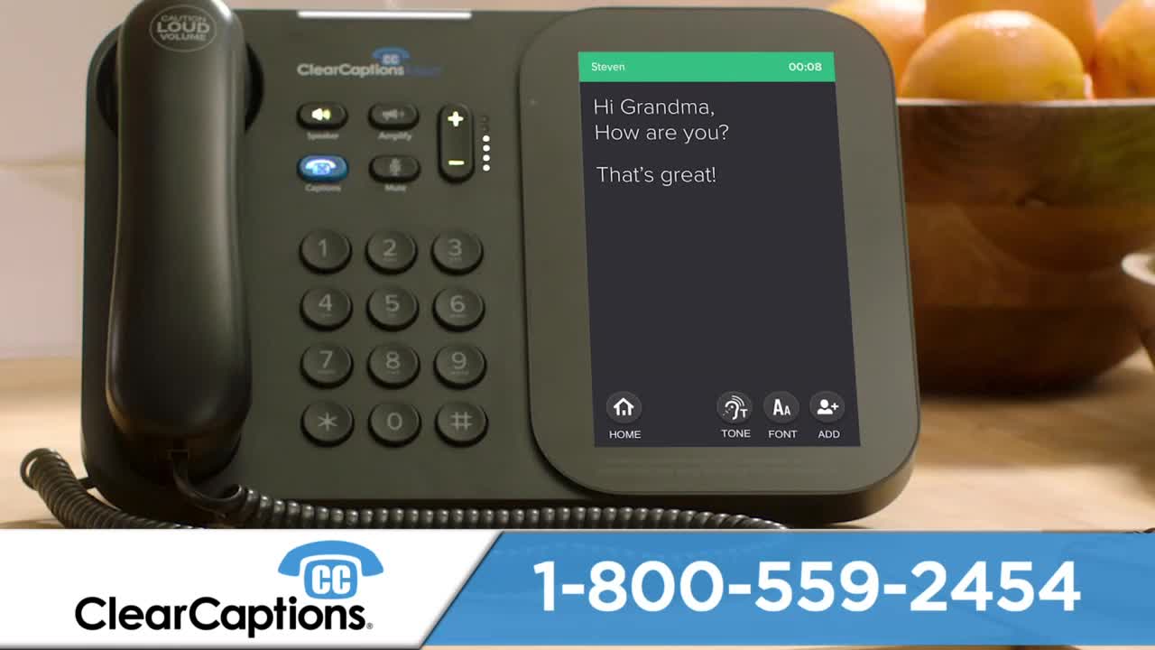 A phone with a screen displays a text conversation: "Hi Grandma, How are you? That's great!" The phone's buttons and screen are lit, and a bowl of oranges sits nearby.
