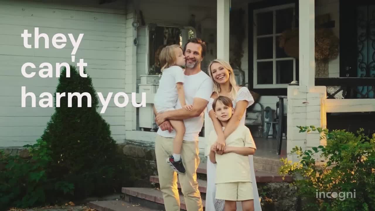 A family of four poses on the porch of their home. The youngest child kisses his father's cheek, while the other son stands with his arms around his mother.
