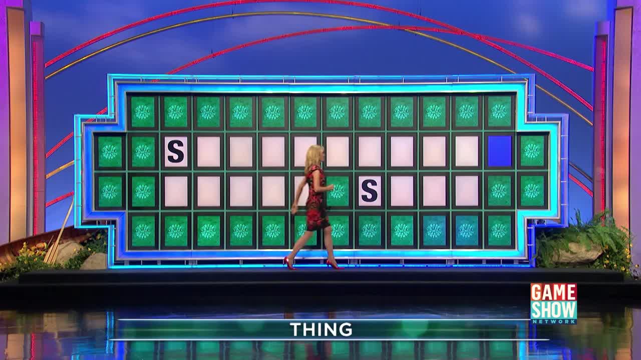 A woman in a red dress walks across the stage, past the puzzle board with the word "THING" partially revealed. Two "S" letters are already lit up on the grid.
