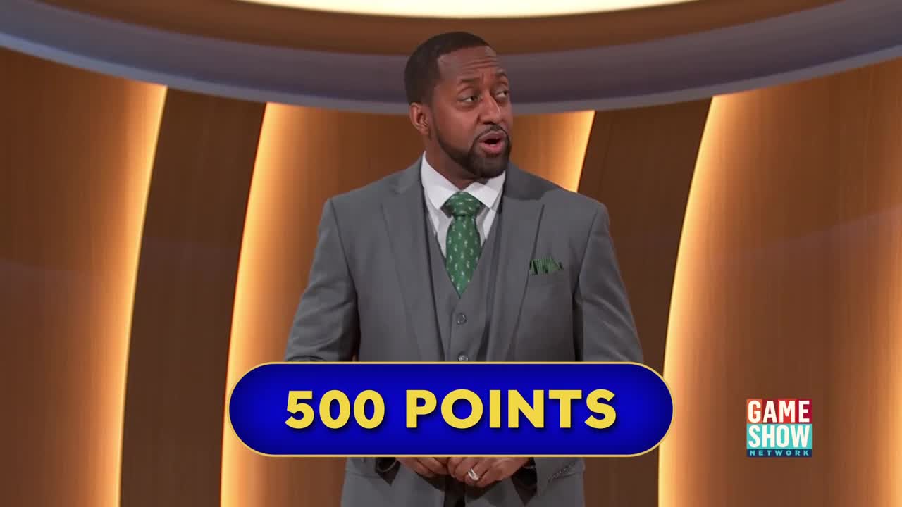 The man in the gray suit, with a green tie, is mid-sentence, looking to his left. A blue and gold banner displays "500 POINTS" in front of him, with the Game Show Network logo in the corner.
