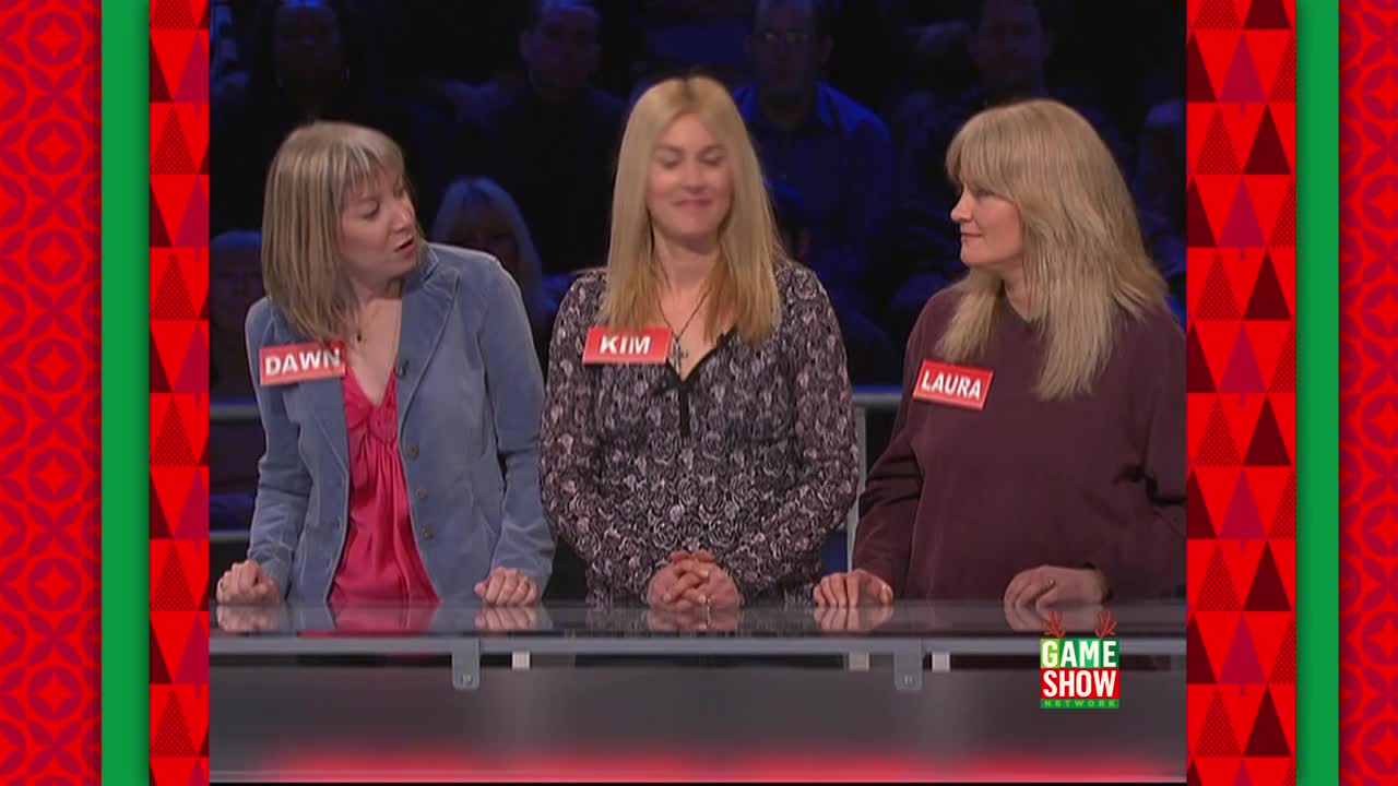 Three women stand behind a sleek, black surface, each wearing a name tag for a game show on the Game Show Network. Dawn, on the left, gestures with her hands as she speaks, while Kim and Laura stand beside her, seemingly listening.
