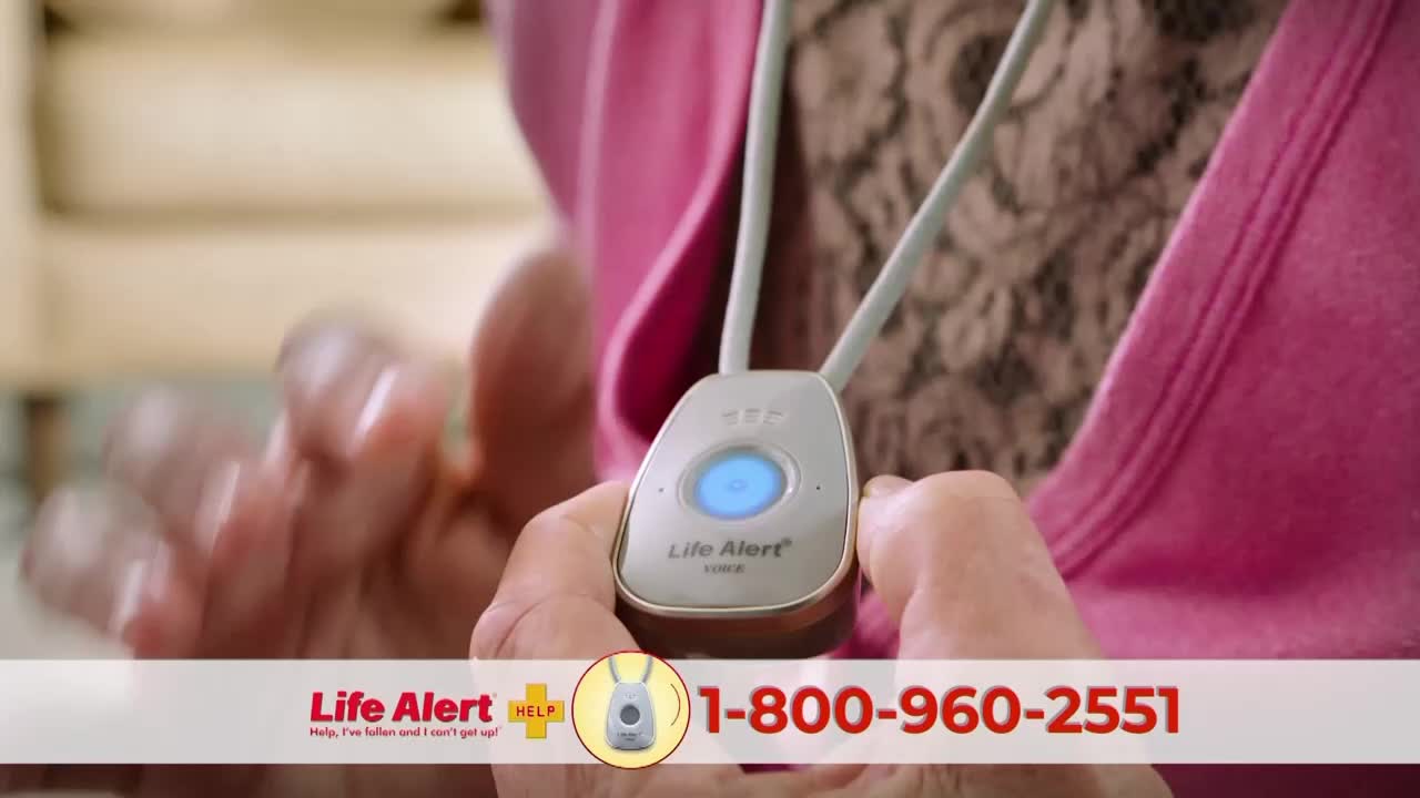 A woman's hands cradle a Life Alert pendant, its blue button glowing. The commercial's phone number is displayed at the bottom of the screen.
