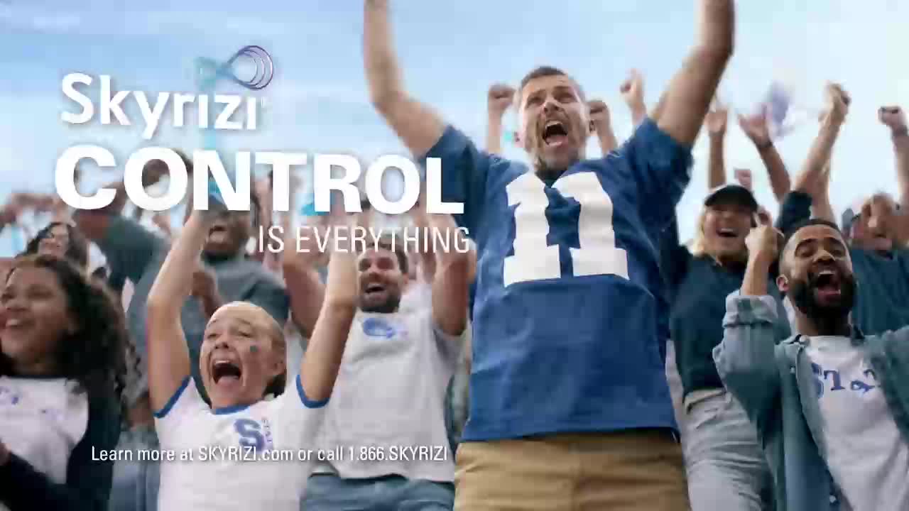 A crowd of fans erupts with joy, their arms raised in celebration. The blue and white jerseys suggest a sports game, likely in the United States.