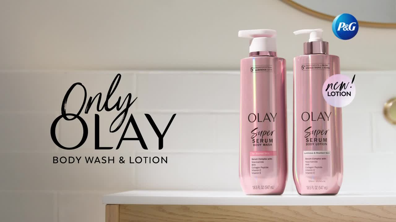 Two tall, shimmering pink bottles stand on a white counter. One bottle reads "OLAY Super Serum Body Wash," and the other says "OLAY Super Serum Body Lotion."