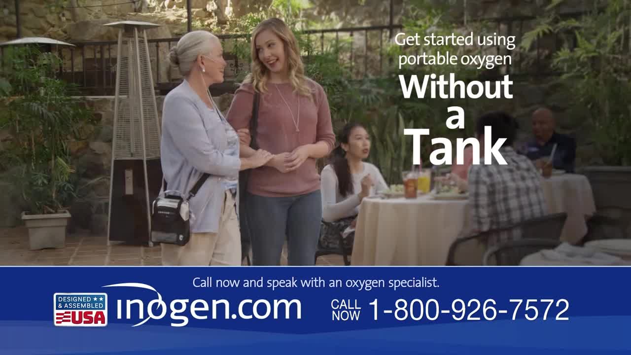 Two women are talking on a patio, one with a portable oxygen concentrator. In the background, a couple dines at a table.