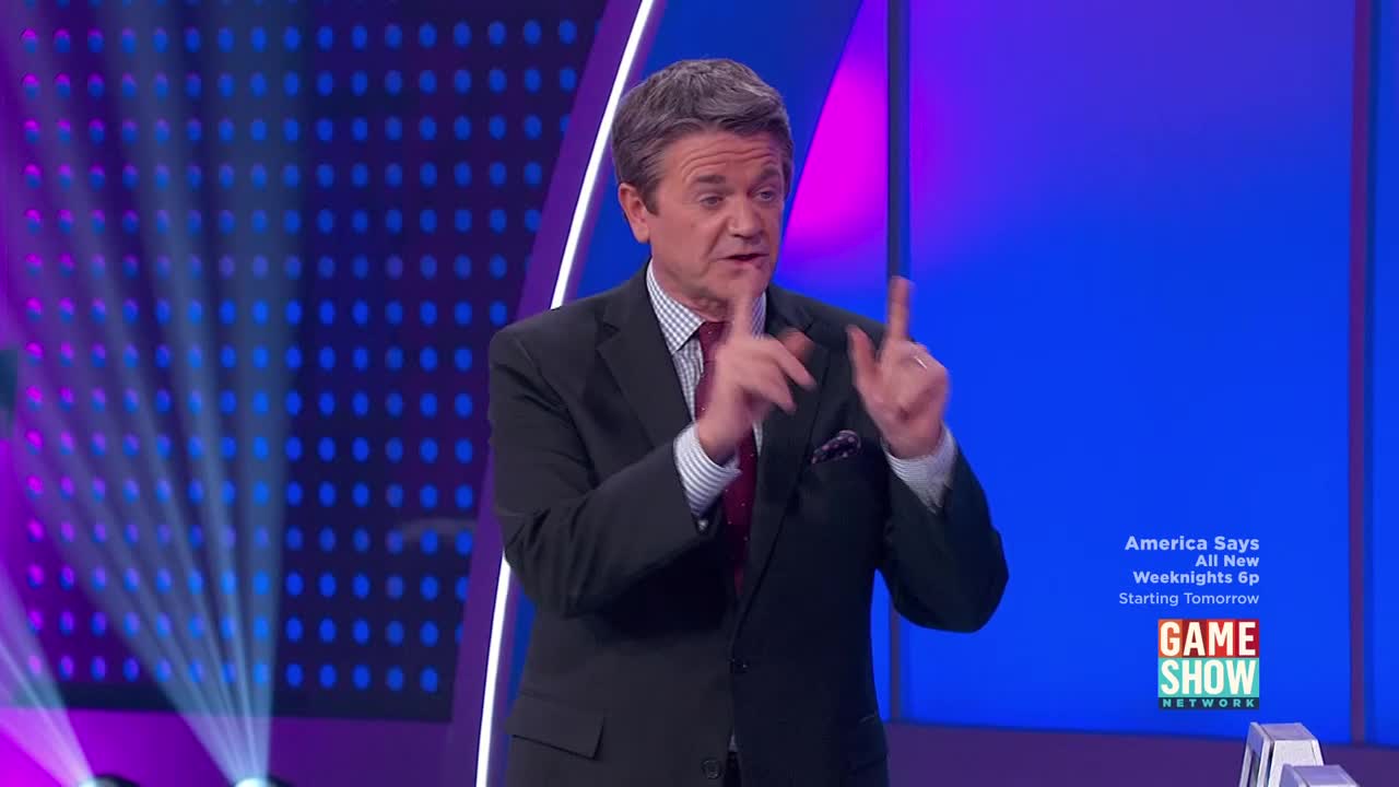 The host on "America Says" gestures with both index fingers raised. A bright blue background with a grid of purple lights pulses behind him.