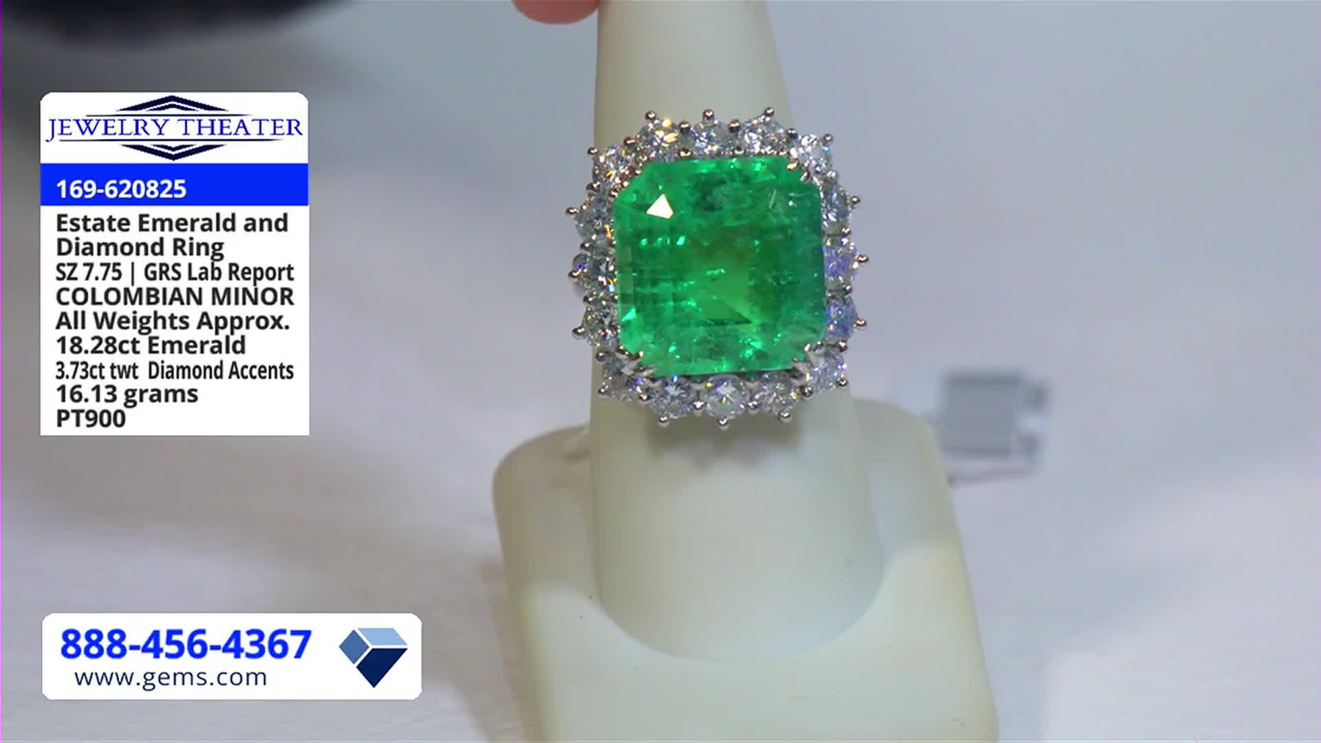 A large, emerald-cut green gemstone ring sits on a white display stand. The ring is surrounded by smaller, clear stones, and a description card is visible in the corner.
