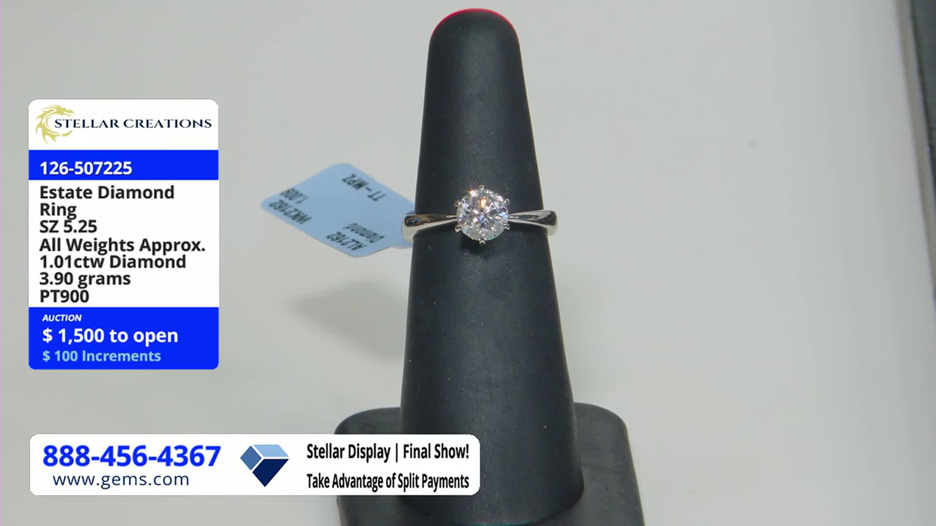 A diamond ring sits on a black display cone, its brilliance catching the light. On the screen, the Gem Shopping Network advertises the ring's auction, starting at $1,500.
