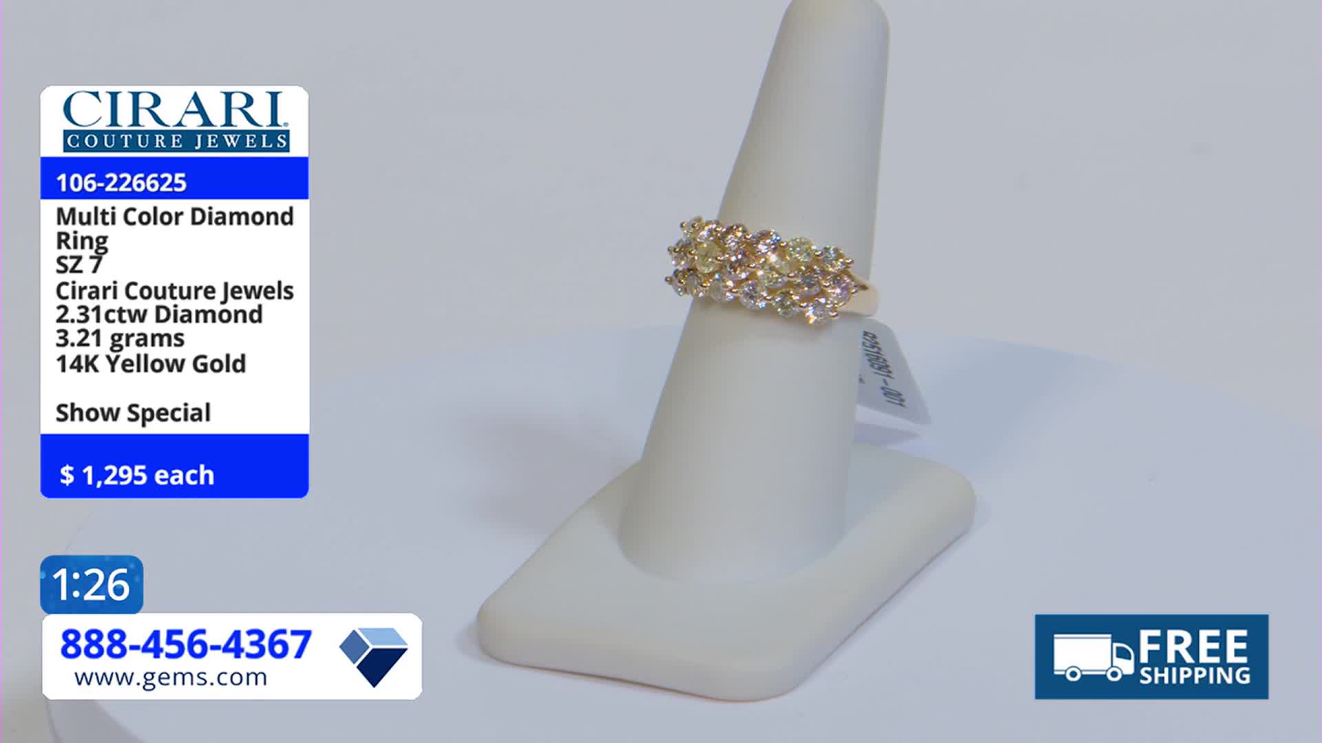 A multi-colored diamond ring sits on a white display stand, lit by studio lights. The Gem Shopping Network logo and price tag are visible in the foreground.

