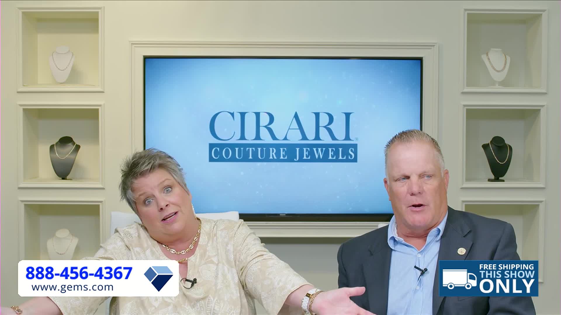 Two people are seated in front of a screen advertising "Cirari Couture Jewels." The woman gestures with her hands while the man beside her speaks, both appearing to be mid-sentence on a Gem Shopping Network broadcast.

