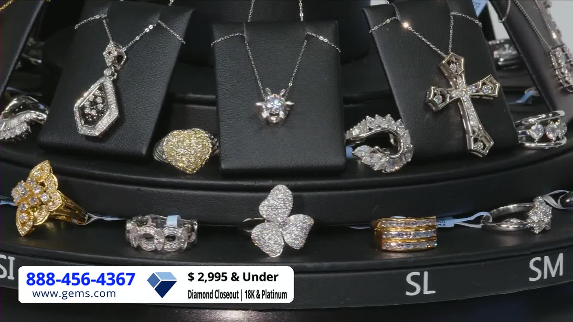 A rotating display showcases various pieces of jewelry, each sparkling under the bright lights. The Gem Shopping Network logo and a phone number are prominently displayed at the bottom.
