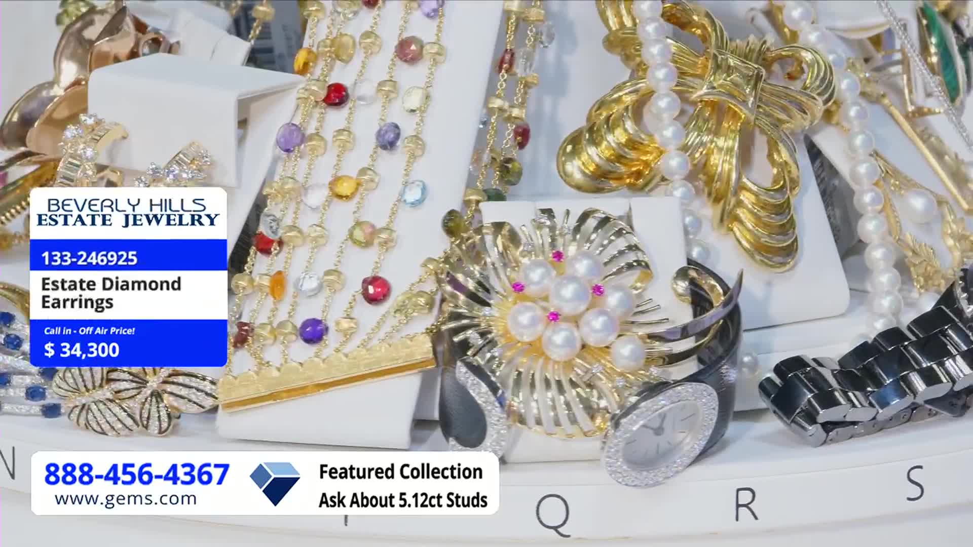 A dazzling array of jewelry, including necklaces and brooches, is arranged on white stands. A blue box at the left advertises "Estate Diamond Earrings" for sale on the Gem Shopping Network in the United States.
