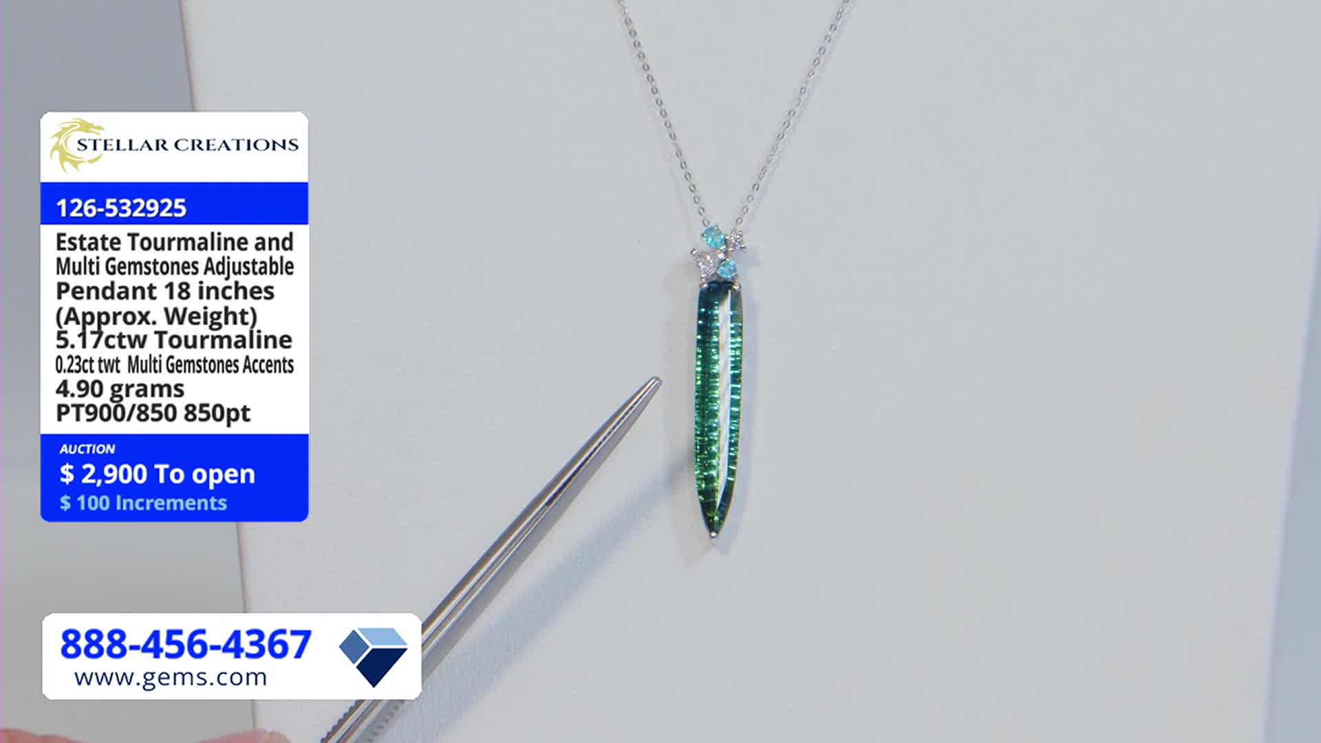 A slender, green tourmaline pendant hangs from a silver chain, displayed against a plain background on Gem Shopping Network.  A pair of tweezers, held by an unseen hand, points at the gemstone.
